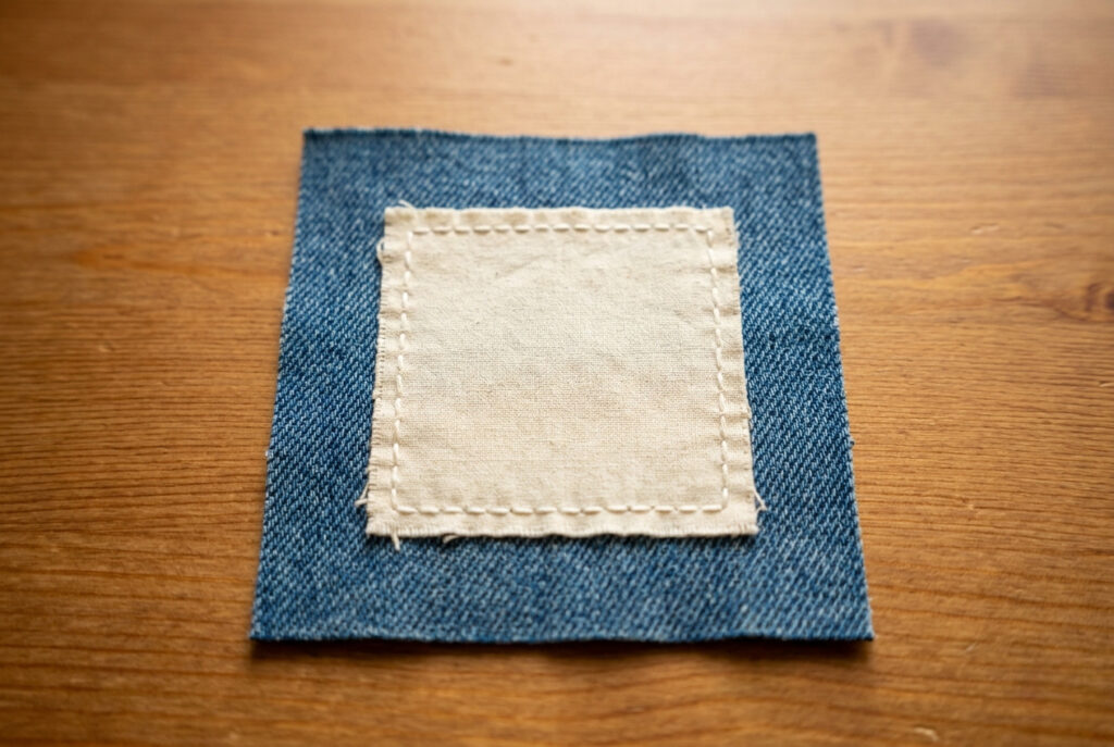 A neatly hand-sewn fabric patch attached to denim cloth with even backstitch around the edges