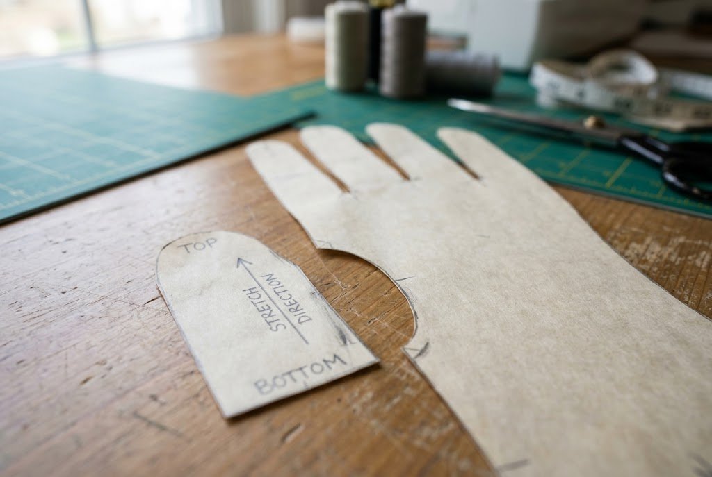 Paper thumb pattern piece labeled with alignment markings next to the main glove pattern