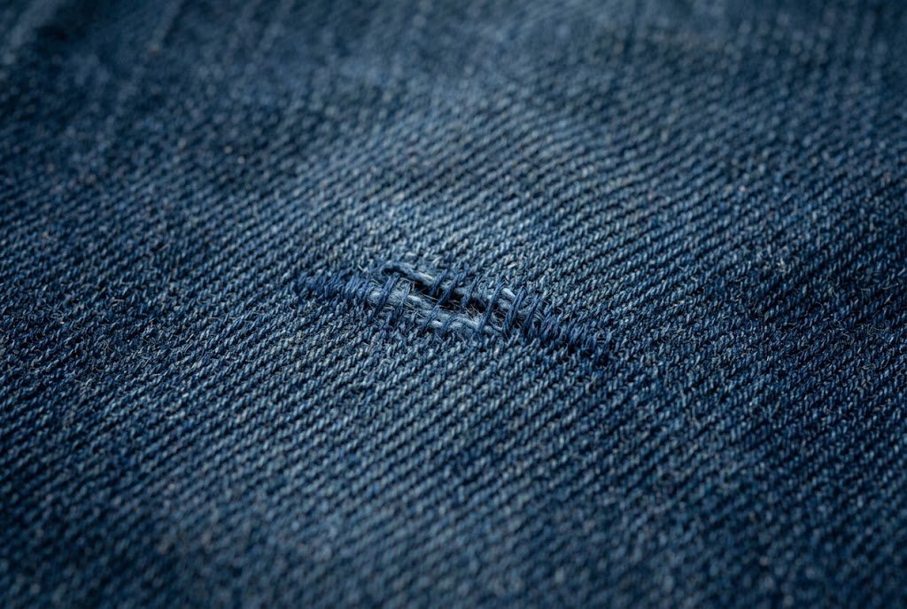 Close-up of a discreet denim repair with thread blending into the fabric