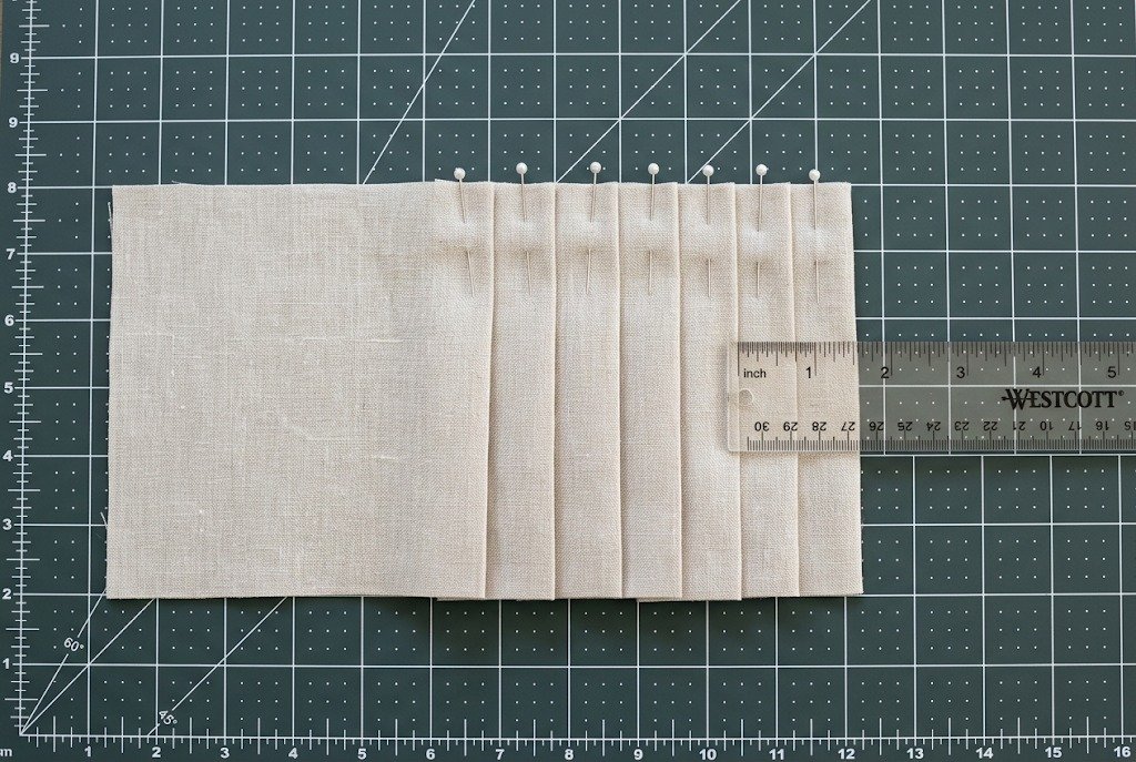 Fabric folded into knife pleats pinned flat on a cutting mat