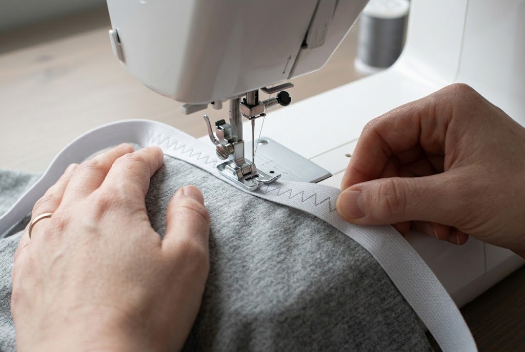 Sewing elastic to knit fabric with a zigzag stitch while gently stretching the elastic between the marks