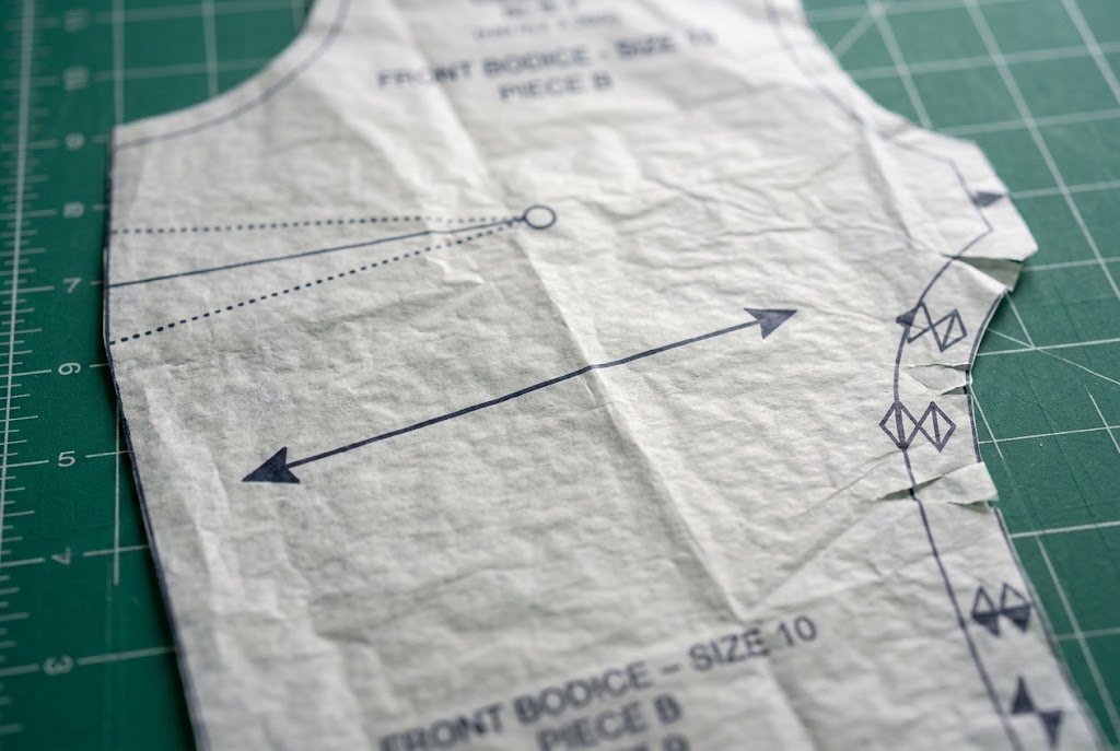 Close-up of a tissue pattern piece showing grainline, notches, and dart markings